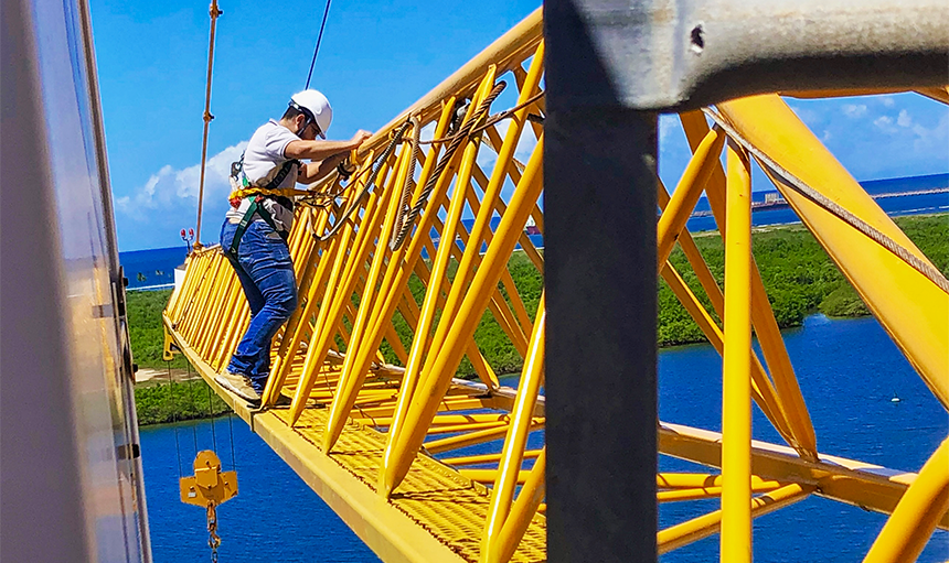 Homem em cima de um guindaste com arnês de segurança e capacete analisando a estrutura.